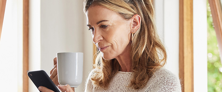 Someone holding a mug and looking at their phone